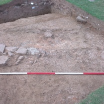 Robbed-out stone wall foundations beyond which is the site of the possible fire place.